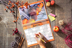 Open wall calendar with rustic October image, female hand ready