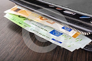 Open wallet with euro cash 10 20 50 100 on a wooden background. Men`s wallet with cash euro.