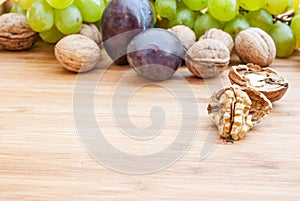 Open walnuts close up on wooden background and grapes and plums in the back