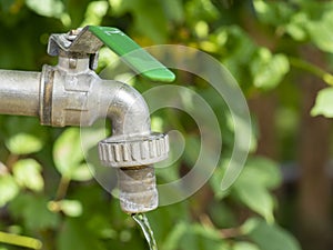 Open water faucet or tap with flowing water in blur garden background