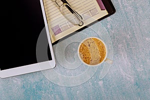 An open weekly notebook and digital tablet eyeglasses on the table a cup of coffee