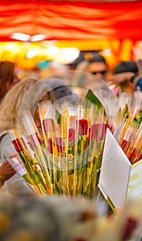 Open white book next to a bouquet of roses at a flower and book stall in a traditional Catalan holiday market with many people