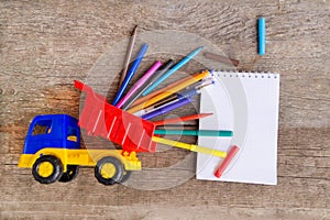 Open white notepad with colorful felt-tip pens and ball pens on the wooden table.
