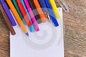 Open white notepad with colorful felt-tip pens and ball pens on the wooden table.