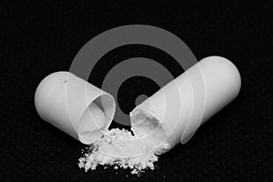 An open white pill on a black background releases white powdery contents