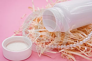 An open white plastic bottle lies on decorative hay close up. The theme of beauty and health. Pink background