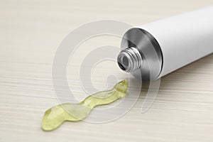 Open white tube with ointment on light wooden table, closeup