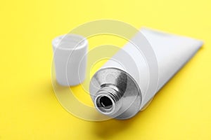 Open white tube of ointment on yellow background, closeup