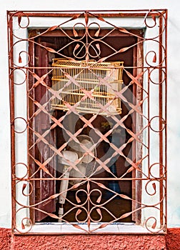 Open window with bird cage and fan behind orange painted metal g