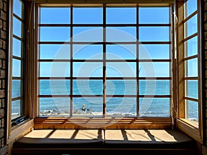 an open window showing a view of the ocean from inside of a brick house