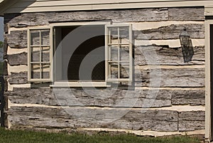 Open window with shutters on exterior wall of original square log cabin