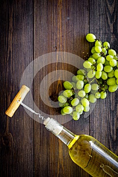 Open the wine concept. Corkscrew into cork of white wine bottle near bunch of grapes on dark wooden background top view