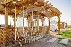 Open wooden bar, cafe, terrace with rope swing for visitors on sand beach, tropical sea resort.Summer vacation on warm