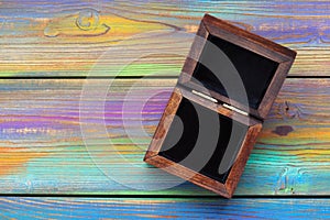 Open wooden jewelry box with black velvet inside on a bright colored wooden background