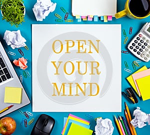 Open your mind. Office table desk with supplies, white blank note pad, cup, pen, pc, crumpled paper, flower on blue