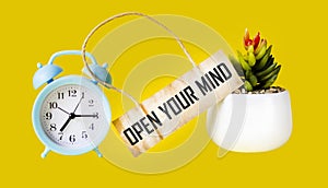 Open Your Mind written on a tag and a yellow background with a clock and a flower