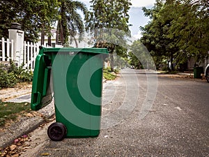 Opened big empty green plastic trash garbage bin in front of the modern house with green trees. No public trash on the