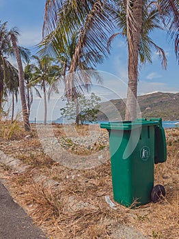 Opened big empty green plastic trash garbage bin in modern comfortable village near sea and palms. Infectious control