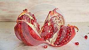 Opened big red pomegranate with seeds on the white concrete bckground. Sliced fresh pomegranate on the light wooden background