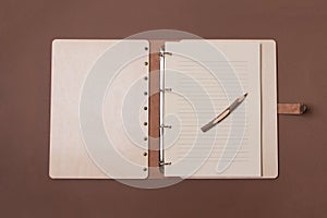 Opened big wooden notebook with pen ready to write on brown colored paper background. Top view