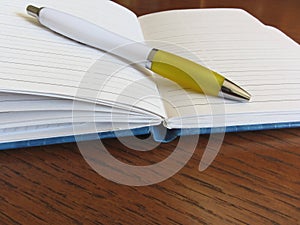 Opened blank lined notebook with pen on wooden table