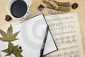 Opened blank notebook with cup of coffee and music notation book, on wooden desktop.