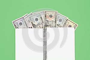 Opened blank notepad and dollar bills on green background, flat lay.