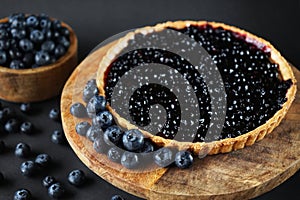 Opened blueberry tart on a wooden stand next to fresh blueberries