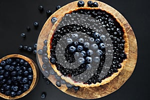 Opened blueberry tart on a wooden stand next to fresh blueberries