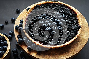 Opened blueberry tart on a wooden stand next to fresh blueberries