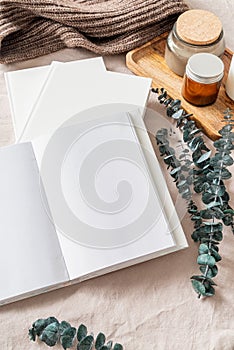 Opened book, candles and eucalyptus leaves top view on white bed. Mock up design