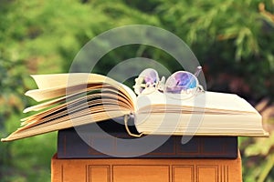 Opened book and glasses lying on stack of books on natural background