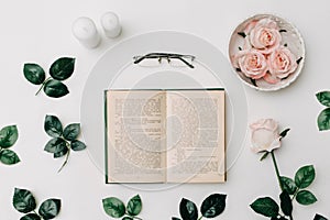 Opened book, glasses, pink roses on white background. Flat Lay