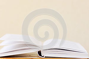 Opened book lying on wooden table blank white wall background. College school university education learning literacy