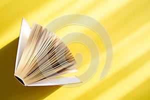 Opened book on a yellow background in the bright sun. The concept of education, reading, buying books. Copy space
