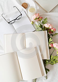 Opened books and flowers top view on white bed. Mock up design