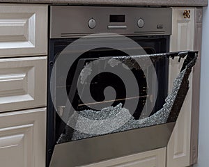 Opened broken oven door in the kitchen, side view, close-up. Broken glass from overheating. Warranty repair