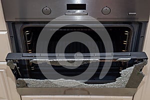 Opened broken oven door in the kitchen, top view, close-up. Broken glass from overheating. Broken glass from impact