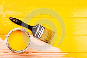 Opened can of paint with brush on yellow freshly painted wooden background.
