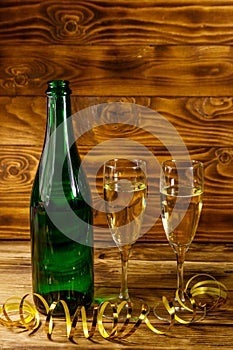 Opened champagne bottle and two glasses of champagne on wooden table