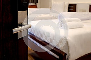 Opened door with blurred background of stack of fresh white bath towels on white bed in hotel room, travel and convenient