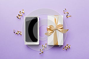 Opened gift box with gold ribbon and smartphone on color background, top view. Blank open box packaging mockup