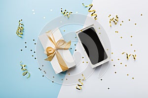 Opened gift box with gold ribbon and smartphone on color background, top view. Blank open box packaging mockup