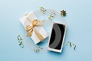 Opened gift box with gold ribbon and smartphone on color background, top view. Blank open box packaging mockup