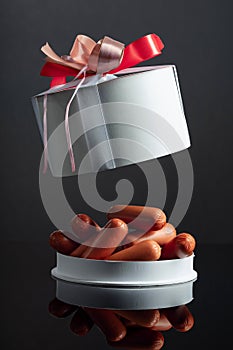 Opened gift box with sausages on a black background