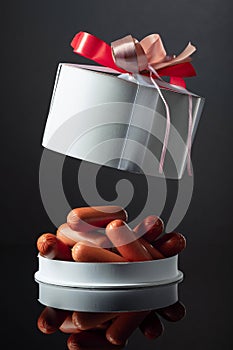 Opened gift box with sausages on a black background