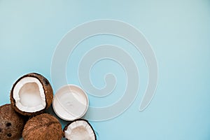 Opened glass jar with fresh coconut oil and ripe coconuts on blue background.