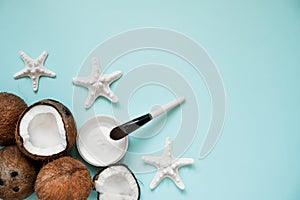 Opened glass jar with fresh coconut oil and ripe coconuts on blue background. Homemade coconut products