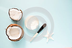 Opened glass jar with fresh coconut oil and ripe coconuts on blue background. Organic healthy food concept. Beauty and SPA concept