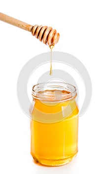 Opened honey jar on white background with wooden honey dipper on top and drop honey